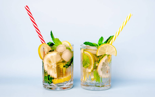 two glasses of lemonade with lime, lemon and mint leaves, ice cubes and straws on white - Foto, afbeelding