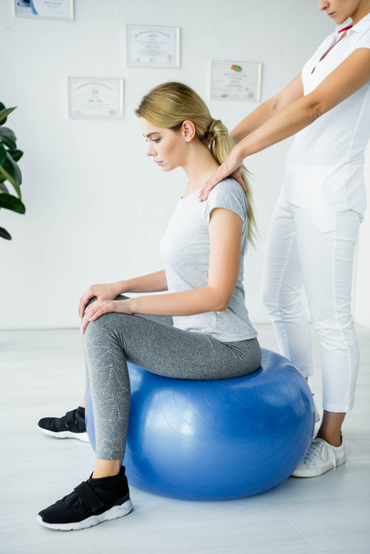 chiropractor touching shoulders of attractive patient on blue exercise ball - Fotografie, Obrázek
