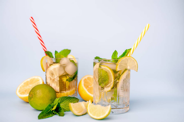 two glasses of lemonade with lime, lemon and mint leaves, ice cubes and straws on white - Фото, изображение