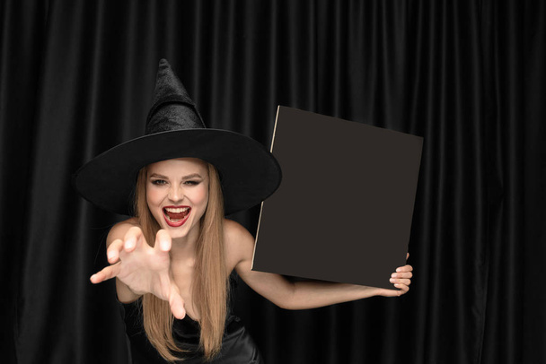Young woman in hat as a witch on black background - Фото, зображення