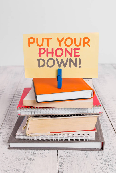 Conceptual hand writing showing Put Your Phone Down. Business photo text end telephone connection saying goodbye caller pile stacked books notebook pin color reminder white wooden. - Photo, Image