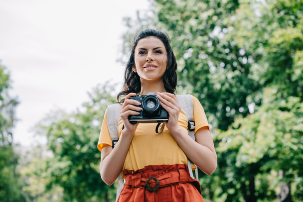 Wesoła młoda kobieta trzyma aparat cyfrowy na zewnątrz  - Zdjęcie, obraz