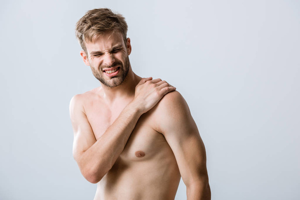 Hemdloser bärtiger Mann mit Schmerzen in der Schulter isoliert auf grau - Foto, Bild