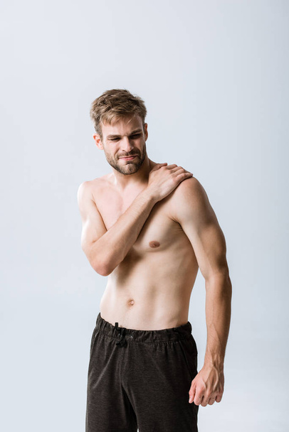 hemdloser bärtiger Sportler mit Schmerzen in der Schulter isoliert auf grau - Foto, Bild