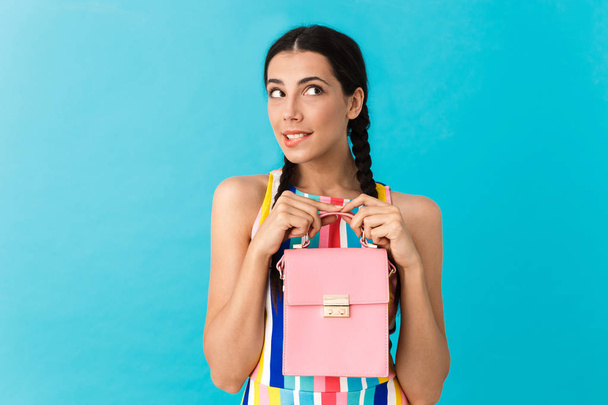 Image of thoughtful caucasian woman with pigtails holding pink bag and biting her lip - Foto, Imagen