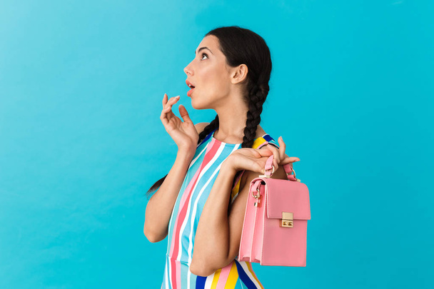 Image of thinking brunette woman with pigtails looking upward while holding pink bag - Foto, afbeelding