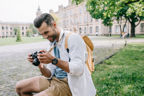 happy man looking at digital camera while sitting near university  - Foto, Bild
