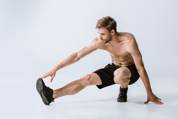 shirtless bearded man in black sneakers stretching on grey - Фото, изображение