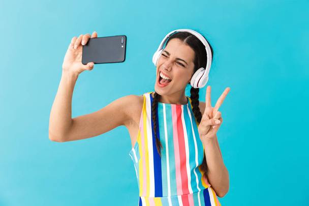 Image of brunette beautiful woman wearing headphones winking while using cellphone - Фото, изображение