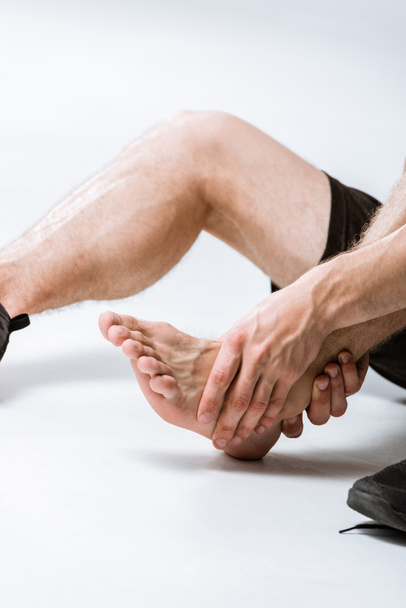 partial view of sportsman with ankle pain on grey - Zdjęcie, obraz