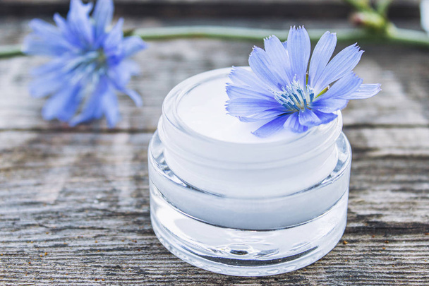 Flor de achicoria azul y crema facial en un frasco de vidrio sobre una vieja mesa de madera. Concepto de salud
. - Foto, Imagen