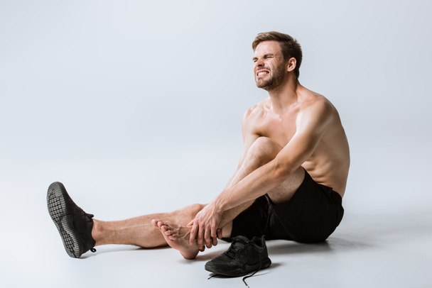 shirtless bearded sportsman with ankle pain on grey - Zdjęcie, obraz