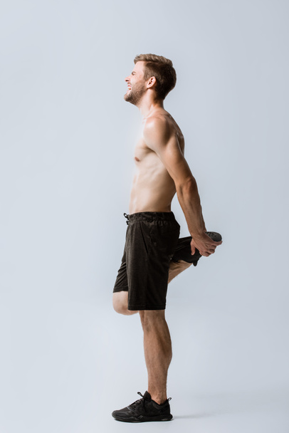 vista completa del deportista sin camisa sintiendo dolor mientras se calienta en gris
 - Foto, Imagen