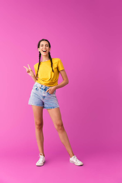Full length photo of young joyful woman wearing denim shorts winking and gesturing peace sign - Photo, image