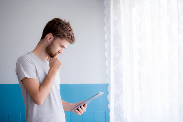 Closeup view of pensive bearded man using tablet while standing  - Фото, изображение