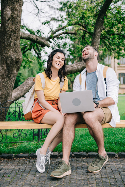 heureuse jeune femme assise sur le banc près de l'homme en utilisant un ordinateur portable
  - Photo, image