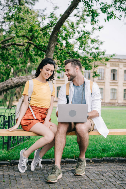 jovem mulher sentada no banco perto do homem usando laptop
  - Foto, Imagem