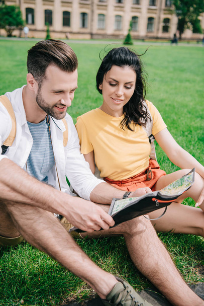 szczęśliwy mężczyzna i kobieta siedzi na trawie i patrząc na mapę  - Zdjęcie, obraz