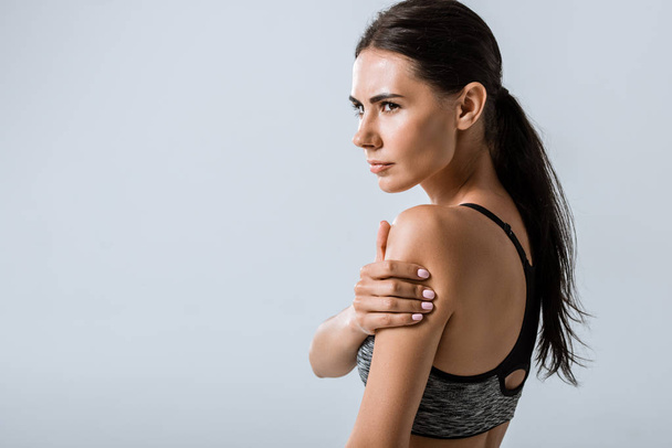 attractive brunette sportswoman with arm pain isolated on grey - Zdjęcie, obraz