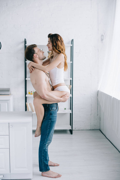 side view of handsome boyfriend holding attractive girlfriend in apartment  - Fotó, kép