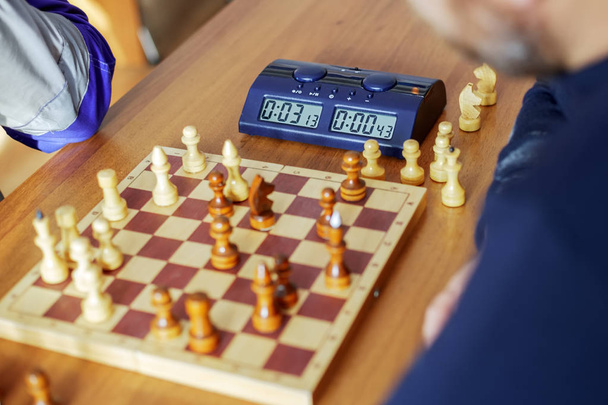 Een elektronische schaak klok en een schaakbord met stukken staan op tafel. - Foto, afbeelding