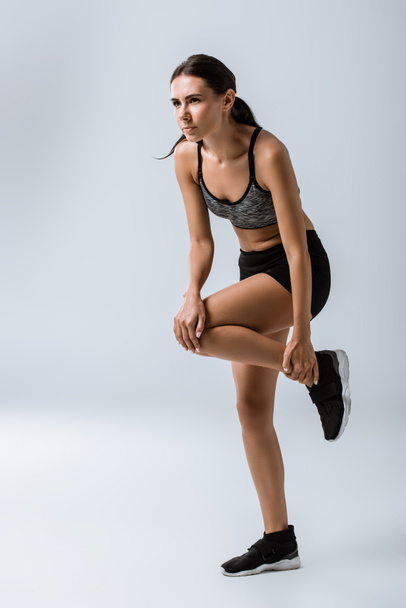 full length view of sportswoman feeling knee pain while warming up on grey - Фото, зображення