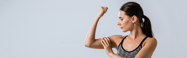 panoramic shot of attractive sportswoman touching muscle isolated on grey - Valokuva, kuva