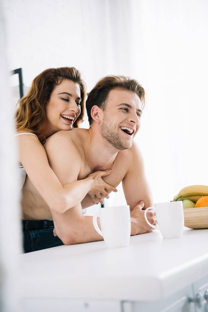 attractive girlfriend and handsome boyfriend smiling and hugging in apartment  - Foto, afbeelding