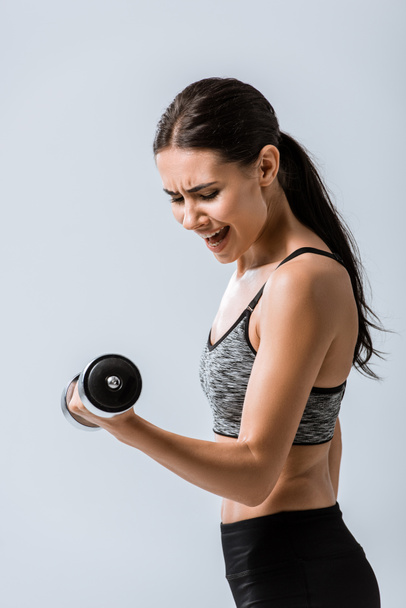attractive brunette sportswoman using dumbbell isolated on grey - Foto, immagini