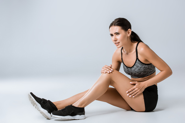 attractive brunette sportswoman with knee pain on grey - Foto, imagen