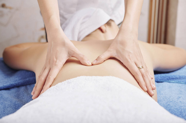 Hände einer Kosmetikerin, die einer Kundin, die auf einem speziellen Bett liegt, professionelle Rückenmassage gibt - Foto, Bild