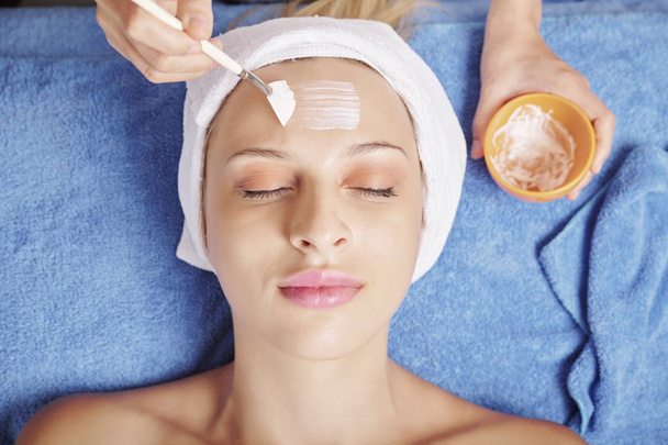 Imagem de close-up de esteticista usando escova ao aplicar máscara natural no rosto de cliente muito feminino
 - Foto, Imagem