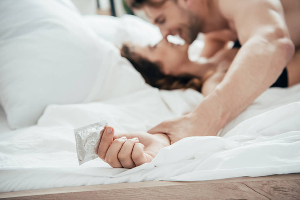 selective focus of woman holding condom and lying in bed  - Φωτογραφία, εικόνα