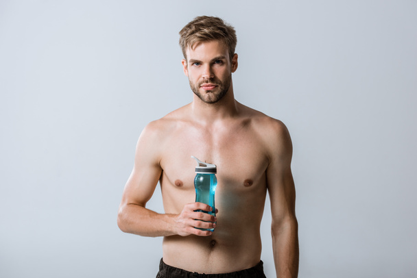 Vooraanzicht van shirtless bebaarde sportman Holding sport fles geïsoleerd op grijs - Foto, afbeelding