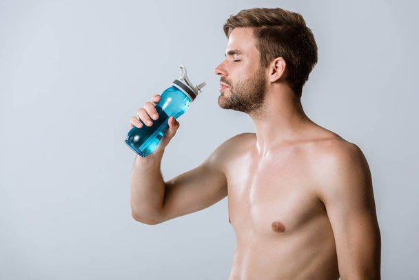 shirtless bearded sportsman holding sport bottle isolated on grey - Fotó, kép