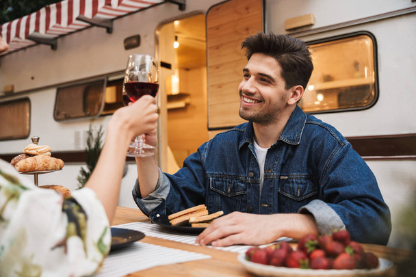 Portrait de couple heureux buvant du vin rouge tout en mangeant des sandwichs ensemble à la table en bois à l'extérieur
 - Photo, image
