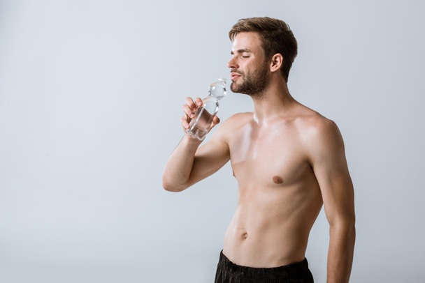 shirtless sportsman drinking water with closed eyes isolated on grey - Foto, imagen