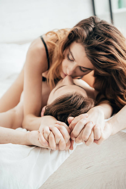 attractive girlfriend in black underwear hugging and kissing boyfriend in bed - Fotografie, Obrázek