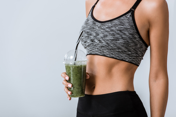 partial view of sportswoman holding smoothie isolated on grey - Fotografie, Obrázek