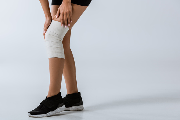 cropped view of sportswoman with elastic bandage on knee on grey - Фото, зображення