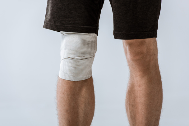cropped view of sportsman with elastic bandage on knee isolated on grey - Fotografie, Obrázek