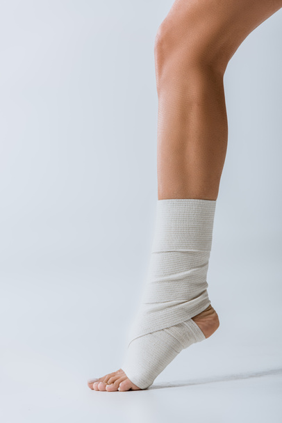 partial view of barefoot girl with elastic bandage on foot on grey - Foto, afbeelding