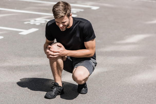 bearded sportsman in black t-shirt with knee pain on street - Photo, Image