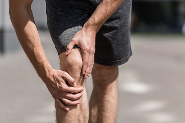 partial view of sportsman with knee pain on street - Fotó, kép