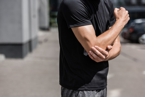 cropped view of sportsman in black t-shirt with elbow pain on street - Photo, Image