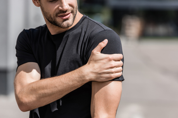 cropped view of sportsman in black t-shirt with shoulder pain on street - Foto, imagen