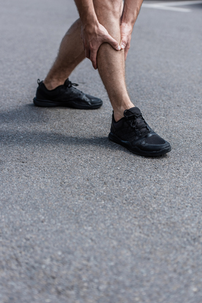 partial view of sportsman in black sneakers with leg pain on street - 写真・画像