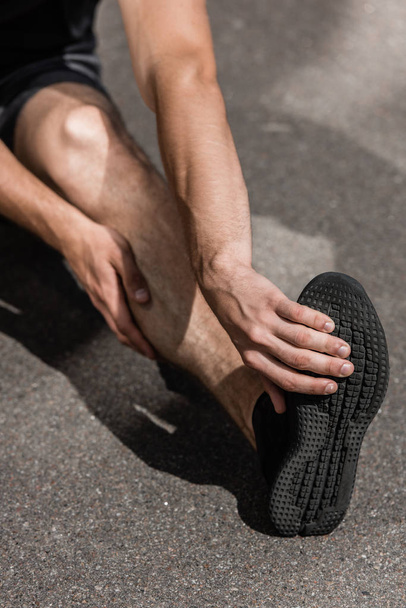 cropped view of sportsman with leg injury on street - Foto, afbeelding