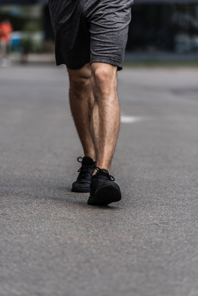 partial view of sportsman in black sneakers walking on street - Foto, afbeelding