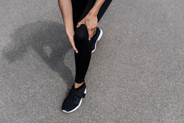 vista recortada de la deportista en zapatillas negras con dolor de rodilla en la calle
 - Foto, Imagen